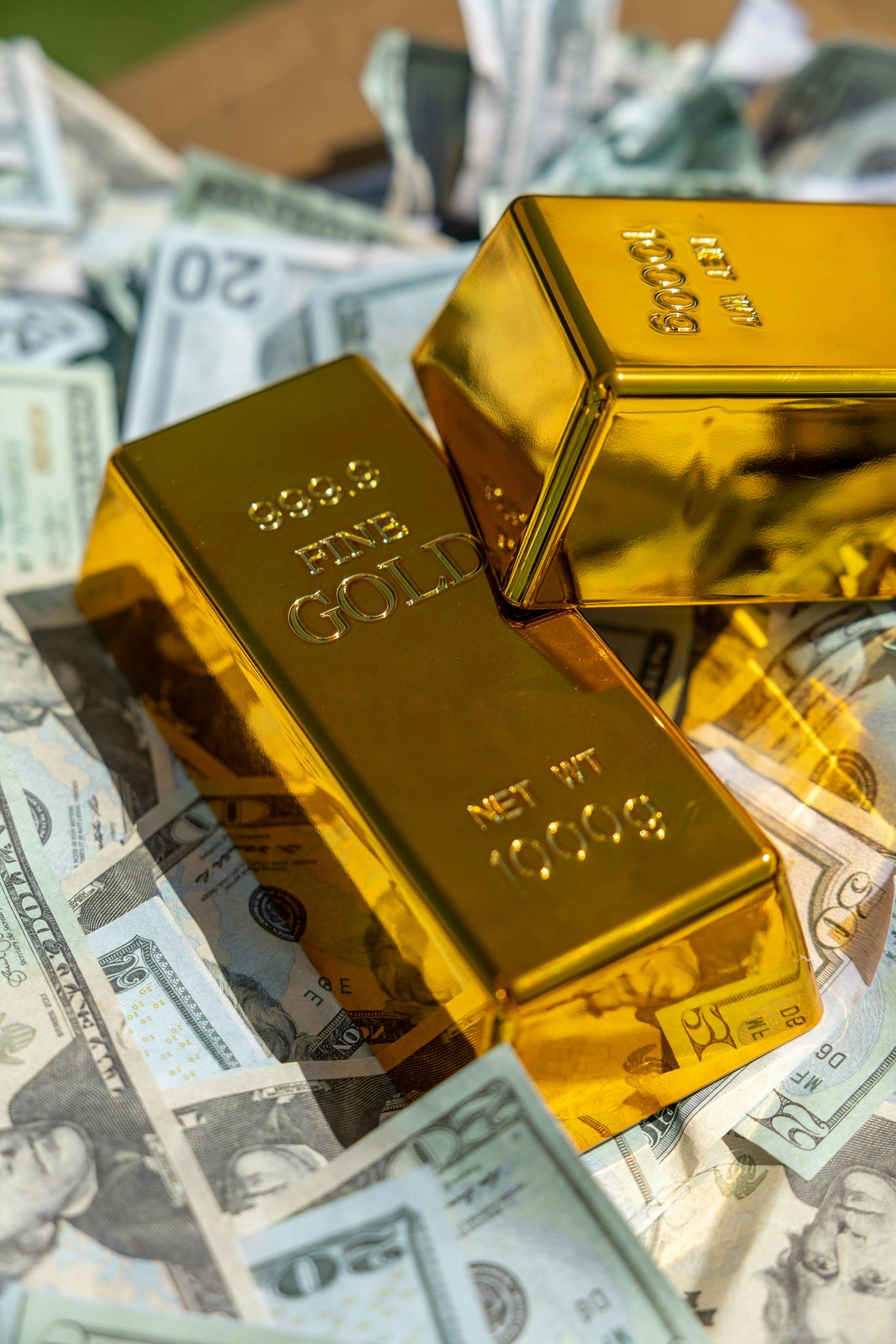 Home Close-up of gold bars atop US currency, symbolizing wealth and investment.