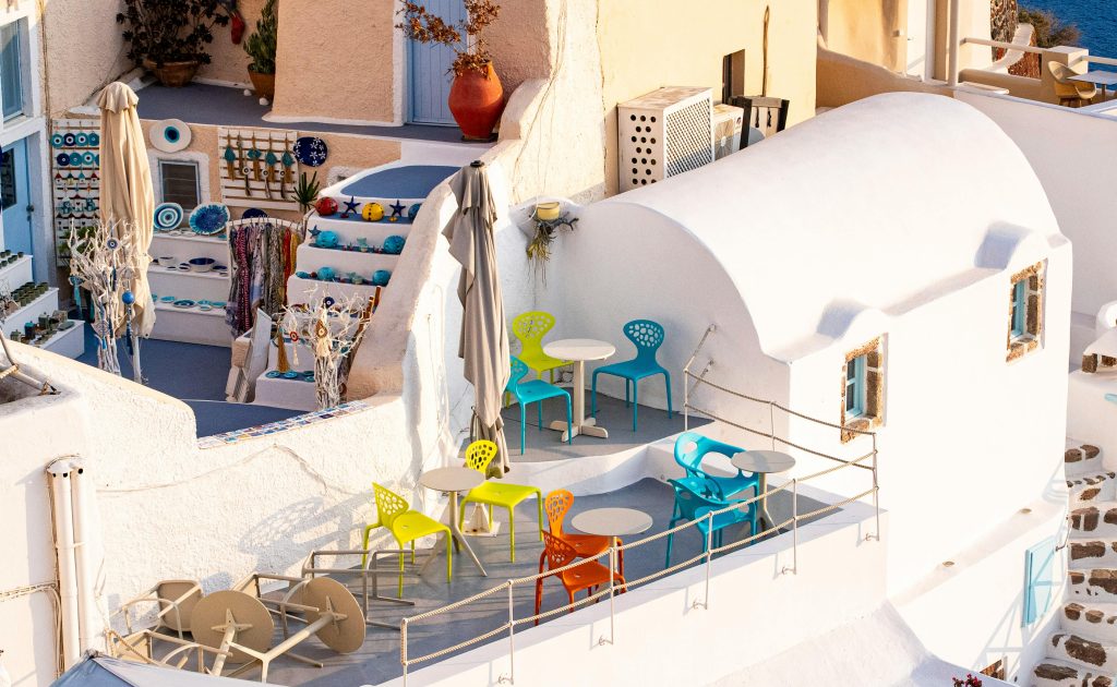 Vibrant rooftop café in Fira, Santorini with colorful chairs and characteristic cycladic architecture.